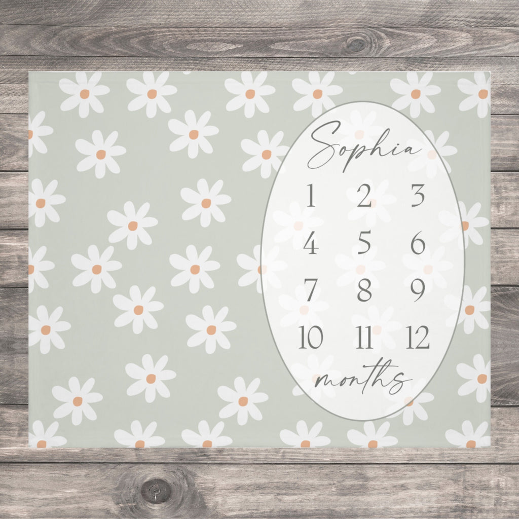 Never miss a moment with ELLO HOME BABY milestone blankets! This Cozy Daisy Baby Milestone Blanket is adorned with elegant Floral Daisies on a neutral sage green design.  An adorable photo backdrop for baby girl's monthly photos to track baby's Growth. A timeless baby keepsake to cherish for years to come! This is a sage green baby milestone blanket with a white daisy pattern. The blanket has a white oval with the name "Sophia" and numbers 1-12 for each month.
