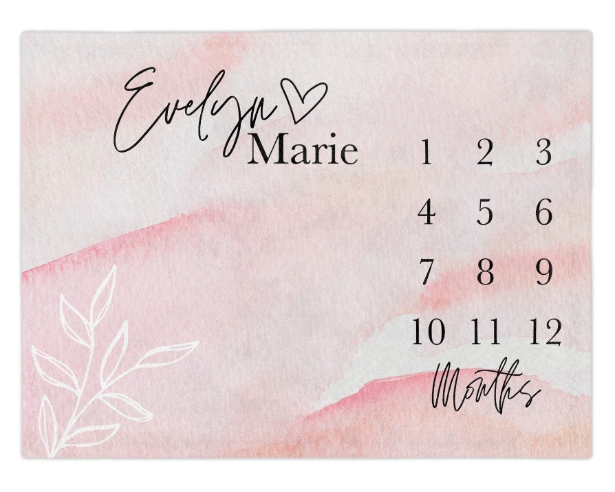 May include: A pink and white watercolor background with a white floral design. The text "Evelyn Marie" is written in black cursive with a heart symbol.  Numbers 1 through 12 are written in black below the name, with the word "Months" written below the numbers. Perfect for baby girls, baby showers, baby sprinkle, newborn gifts, or expecting parents who love soft, modern nursery aesthetics.