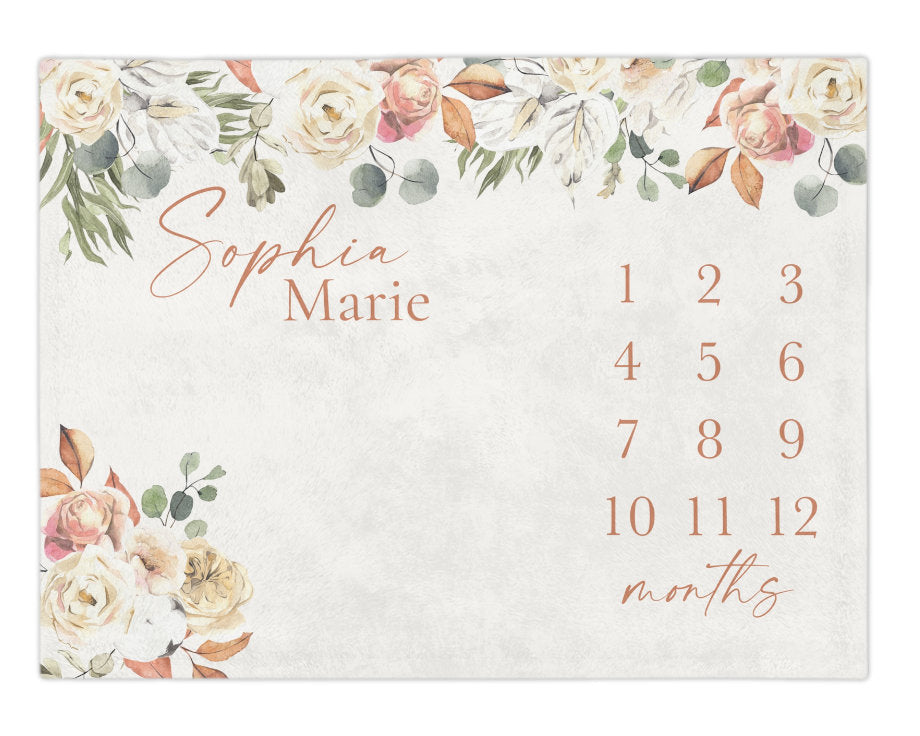 A boho milestone blanket featuring a light gray background with a floral border of cream, peach, and green leaves. The text reads Sophia Marie in script and print, with numbers 1 through 12 and the word months in copper.