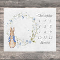 Vintage Rabbit Baby Milestone blanket featuring a watercolor illustration of a blue floral wreath with a Peter Rabbit character in the center. The baby growth chart includes the name "Christopher" and numbers 1 through 12 to track a baby's growth in months.