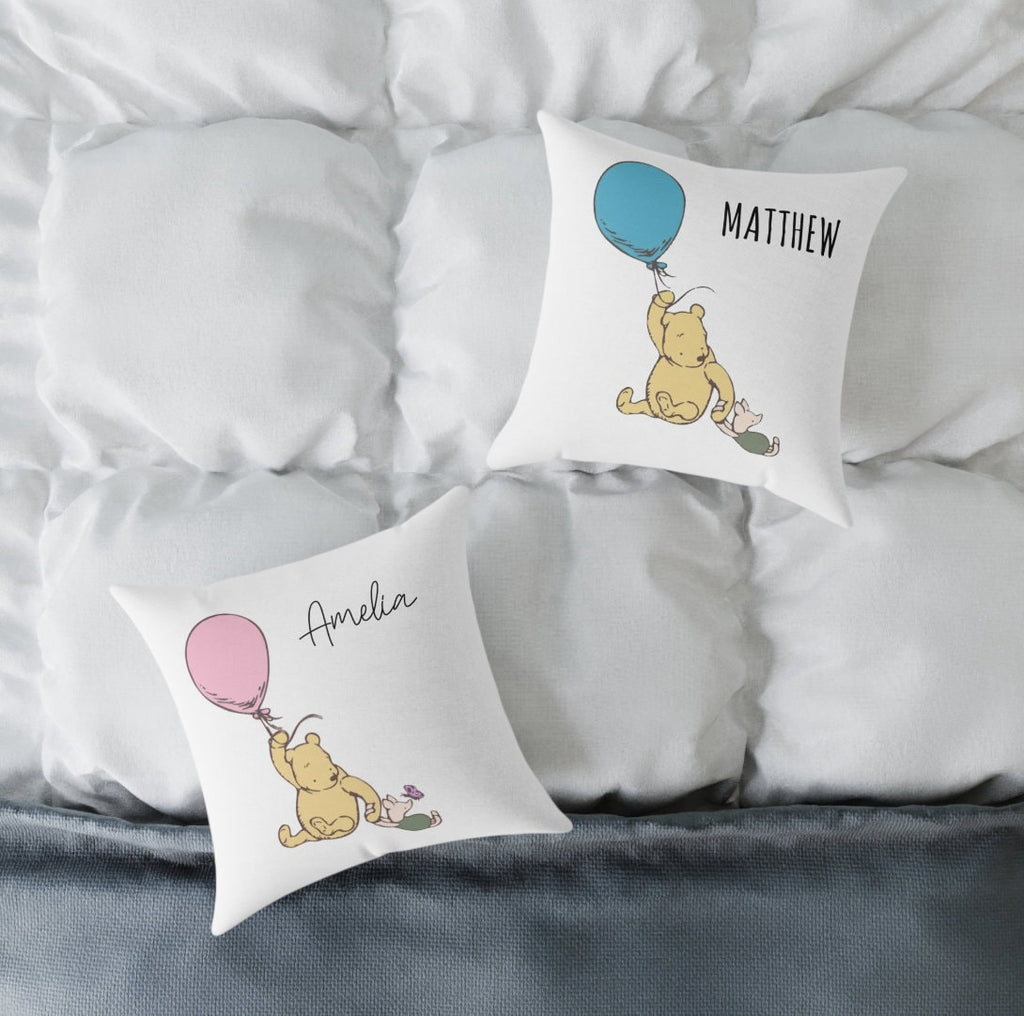 May include: Two white throw pillows with Winnie the Pooh and Piglet holding balloons. The pillow on the left has a pink balloon and the text "Amelia". The pillow on the right has a blue balloon and the text "MATTHEW".