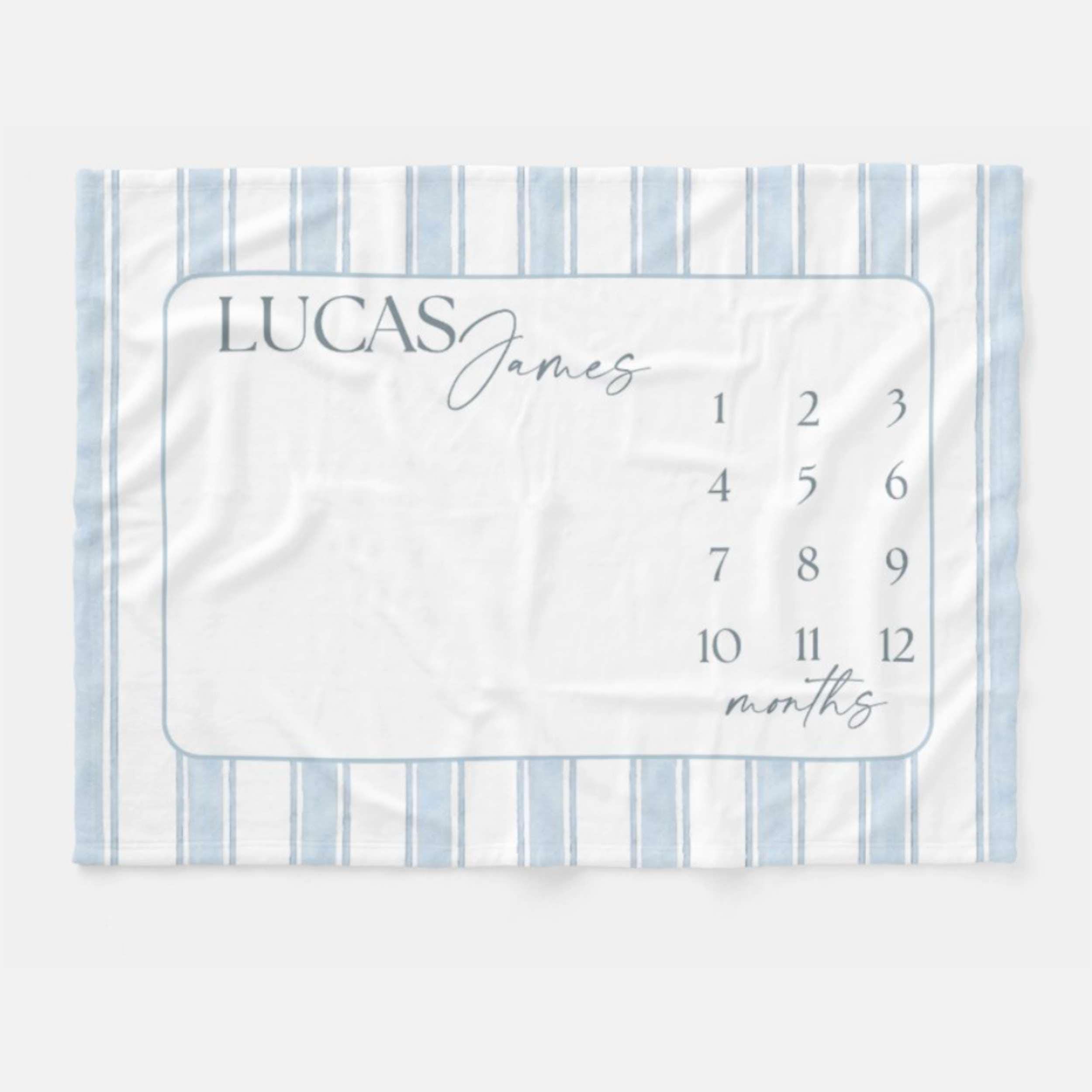 Personalized Blue Heirloom Stripe Baby Milestone Blanket. Baby Milestone Blanket Boy, Month Blanket with Blue Stripes, Preppy Monthly Growth Mat, Custom Baby Shower Gift. A white baby milestone blanket with blue vertical stripes and a rectangular center. The center has the name "LUCAS James" in gray script, with numbers 1-12 and the word "months" in script.
