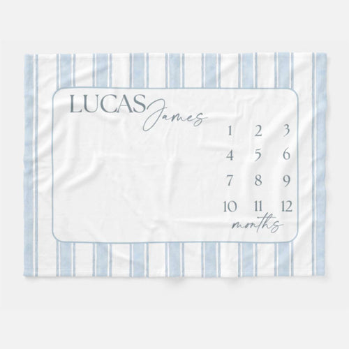 Personalized Blue Heirloom Stripe Baby Milestone Blanket. Baby Milestone Blanket Boy, Month Blanket with Blue Stripes, Preppy Monthly Growth Mat, Custom Baby Shower Gift. A white baby milestone blanket with blue vertical stripes and a rectangular center. The center has the name "LUCAS James" in gray script, with numbers 1-12 and the word "months" in script.