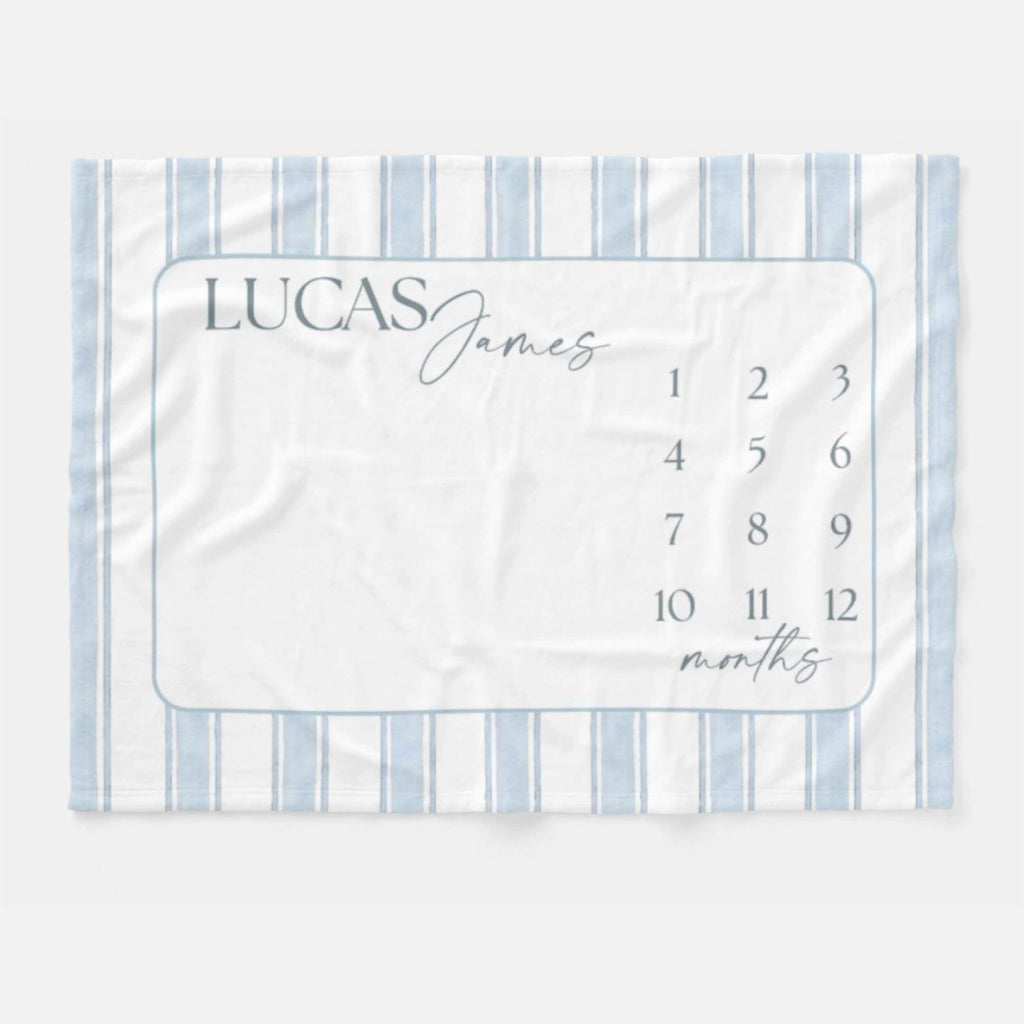 Personalized Blue Heirloom Stripe Baby Milestone Blanket with soft blue watercolor stripes, custom baby name, monthly milestone numbers, realistic brown teddy bear, and smiling baby in a neutral nursery flat lay.