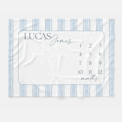 Personalized Blue Heirloom Stripe Baby Milestone Blanket with soft blue watercolor stripes, custom baby name, monthly milestone numbers, realistic brown teddy bear, and smiling baby in a neutral nursery flat lay.