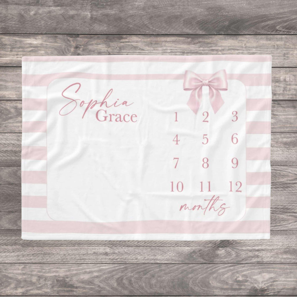 A white and pink milestone blanket with the name in cursive script. The blanket features a pink bow and numbers 1-12 for tracking a baby's growth. Pink stripes border the blanket. Capture the precious journey of your baby girl’s first year with our soft Pink Striped Bow Milestone Blanket. Designed with a trendy coquette aesthetic, delicate pink stripes and a charming watercolor bow, this ultra-soft blanket is the perfect backdrop for those "Insta-worthy" monthly photos from newborn