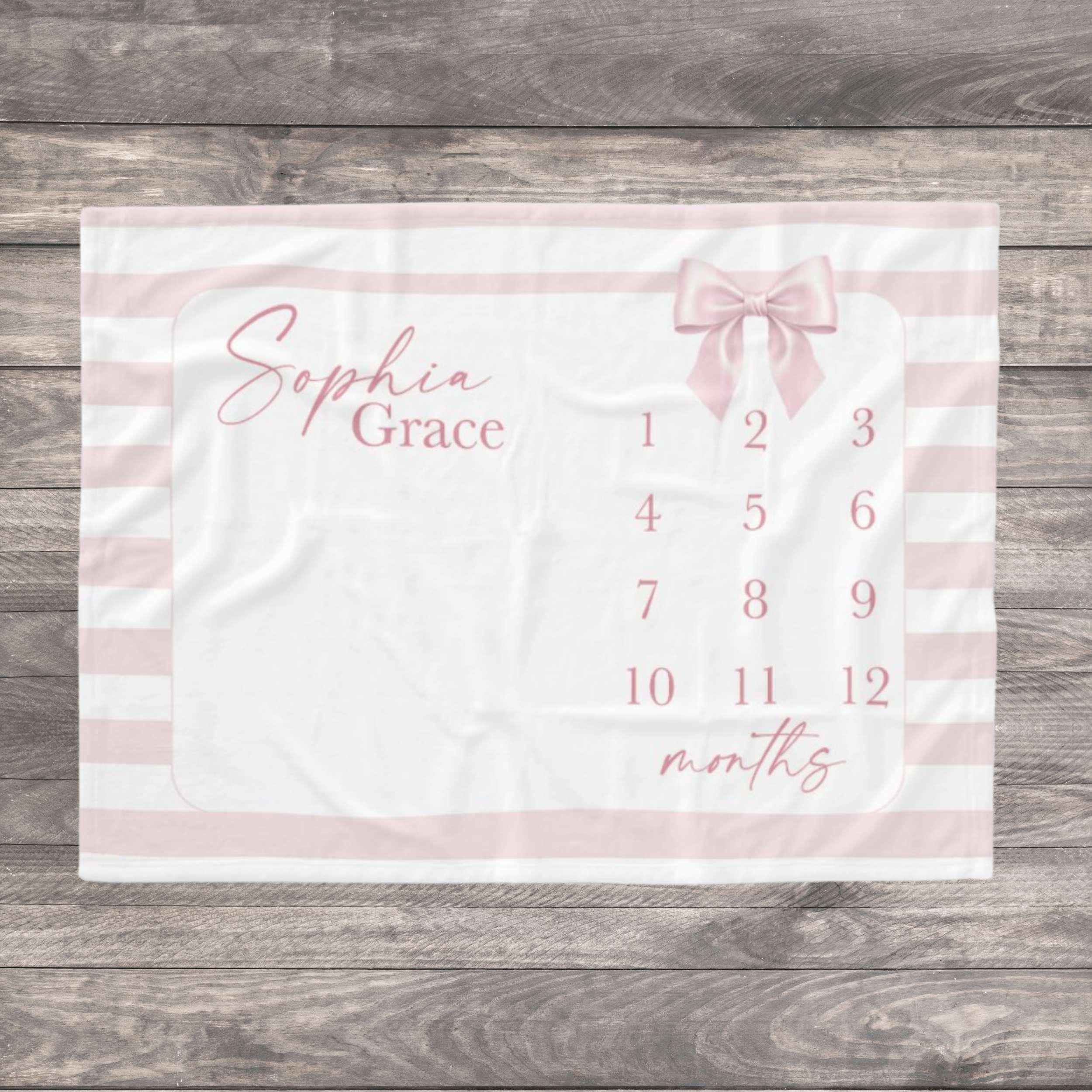 A white and pink milestone blanket with the name in cursive script. The blanket features a pink bow and numbers 1-12 for tracking a baby's growth. Pink stripes border the blanket. Capture the precious journey of your baby girl’s first year with our soft Pink Striped Bow Milestone Blanket. Designed with a trendy coquette aesthetic, delicate pink stripes and a charming watercolor bow, this ultra-soft blanket is the perfect backdrop for those "Insta-worthy" monthly photos from newborn