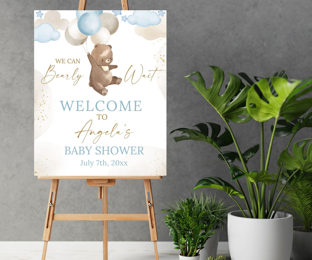 May include: A baby shower welcome sign with a brown bear holding blue and white balloons. The sign says "We can Bearly Wait" and "Welcome to Angela's Baby Shower" with the date "July 7th, 20xx".