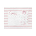 May include: A rectangular baby milestone blanket with a pink and white striped border. The center features a white space with the name "Sophia Grace" in cursive, a pink bow, and numbers 1-12 with the word "months".