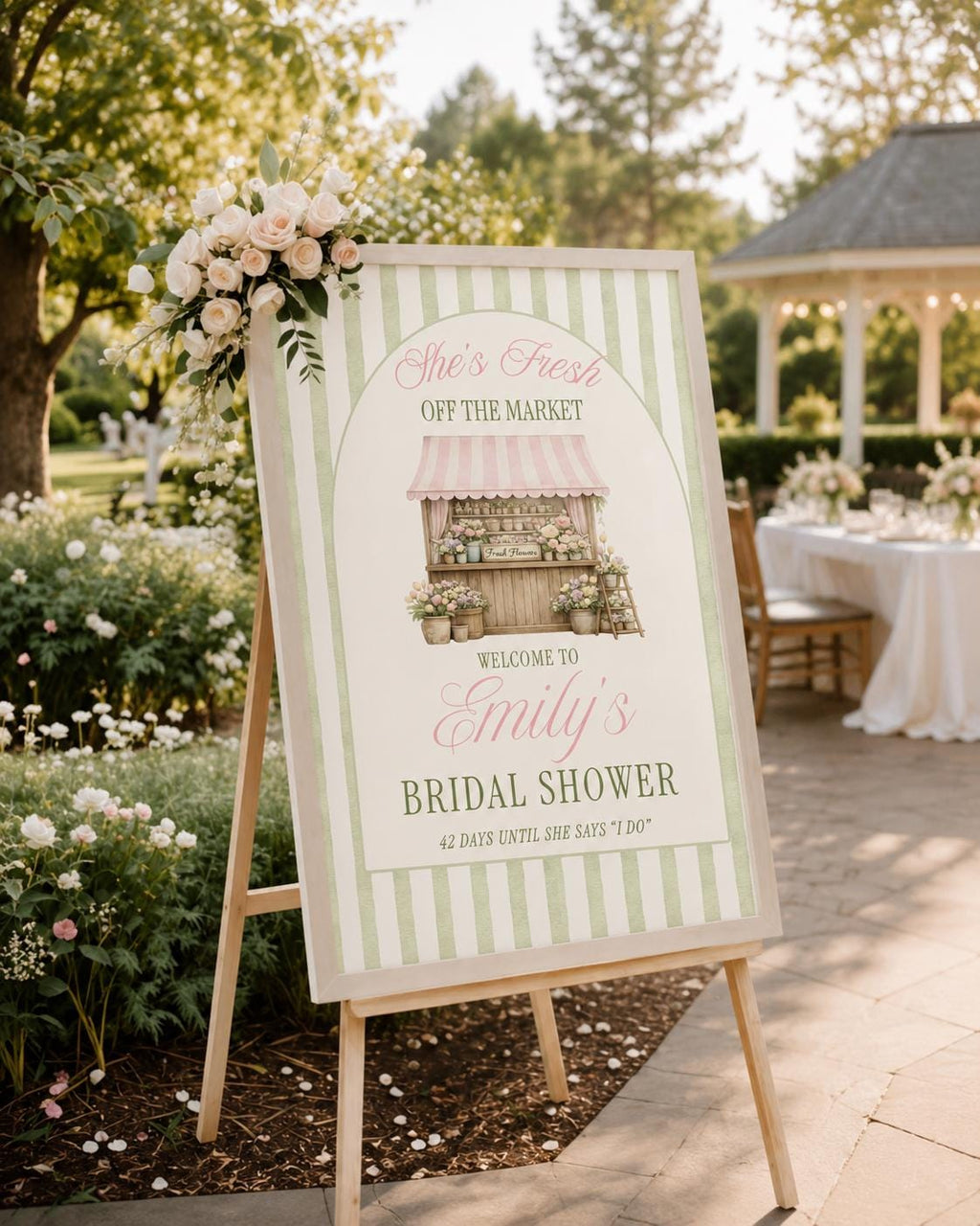 Pink and Green Personalized Fresh Off the Market bridal shower sign displayed in upscale bridal venue with soft natural lighting and timeless decor.  Bridal shower welcome sign on a wooden easel featuring a light green striped border and a floral pink farmer's market.