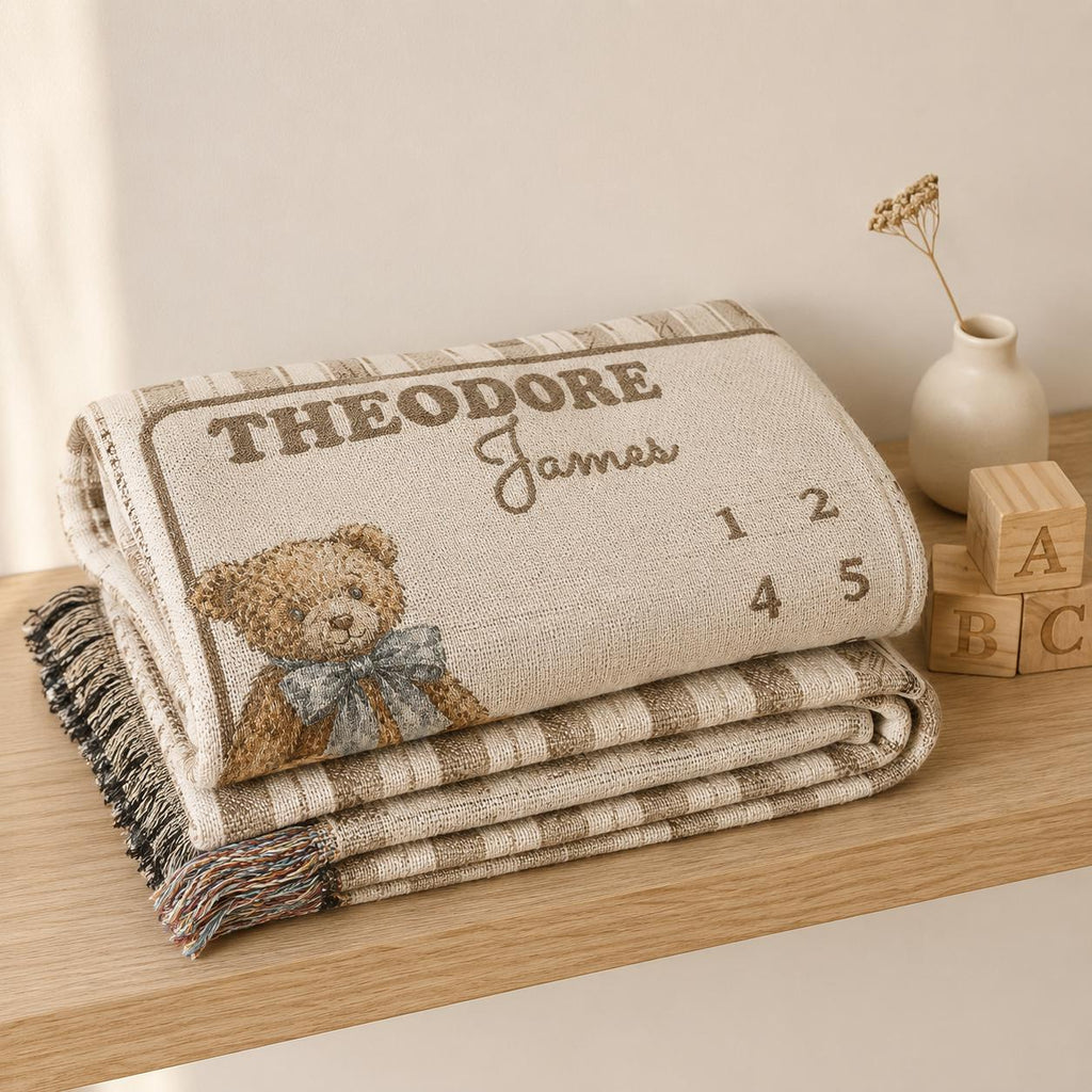 Folded woven cotton baby milestone blanket with brown stripes, teddy bear illustration and custom name.