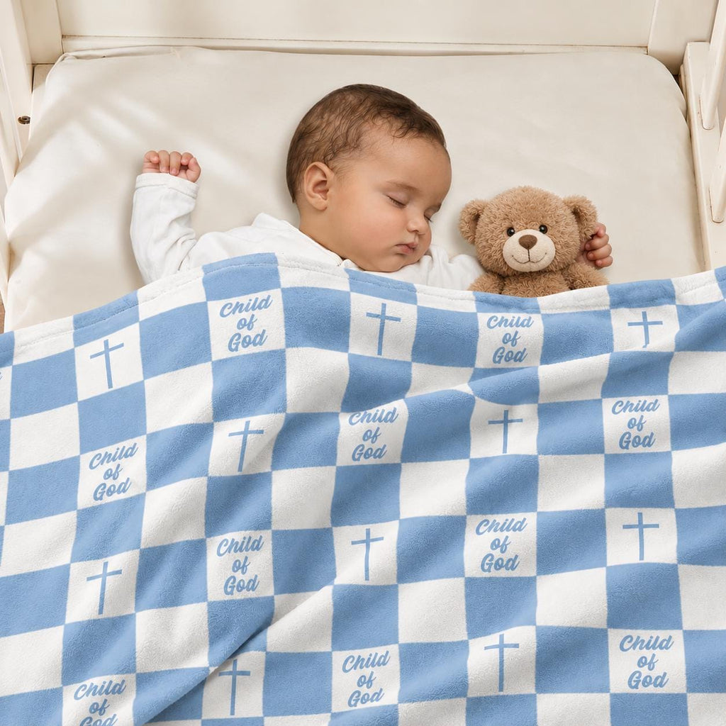 Blue and white Christian baby blanket with Child of God design draped over a sleeping baby in a cozy nursery, featuring a blue gingham pattern with crosses and Child of God lettering, shown with a soft brown teddy bear. ELLO HOME BABY