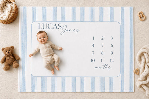 Personalized blue striped baby milestone blanket with watercolor stripes, featuring a soft medium brown teddy bear, neutral nursery styling, and a smiling baby lying on a custom monthly milestone blanket for newborn photos.