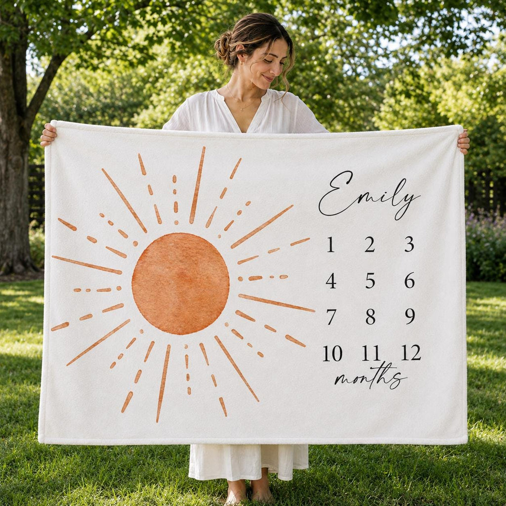Mother displaying a personalized 60 by 50 inch sun milestone blanket outdoors in bright natural light and green surroundings.