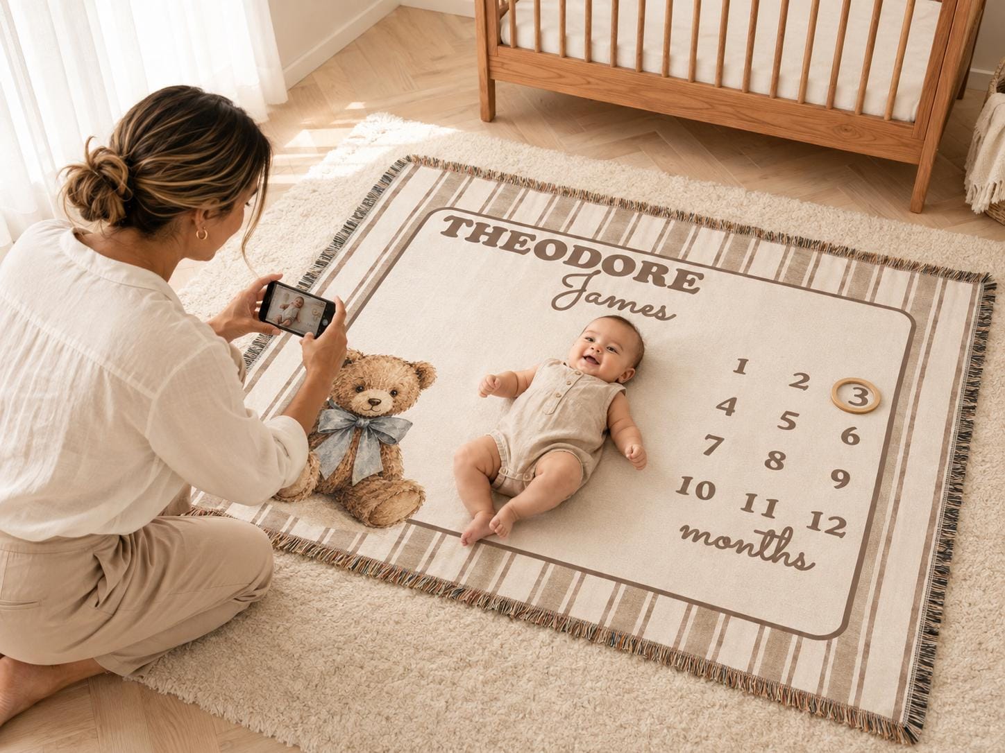Mother photographing baby on a brown striped woven teddy bear monthly milestone blanket in a neutral nursery.