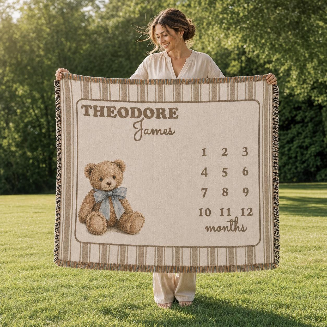 Mother is outdoors holding up a brown striped baby milestone blanket.