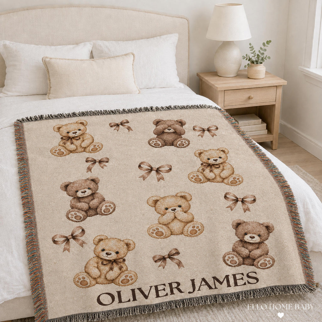 Personalized neutral bear nursery throw draped across a bright bed, featuring woven cream and brown teddy bears, bows and the name Oliver James.