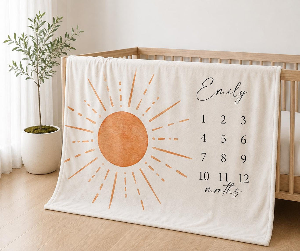 Personalized neutral milestone blanket draped over a light oak crib, featuring a terracotta sun and monthly number grid.
