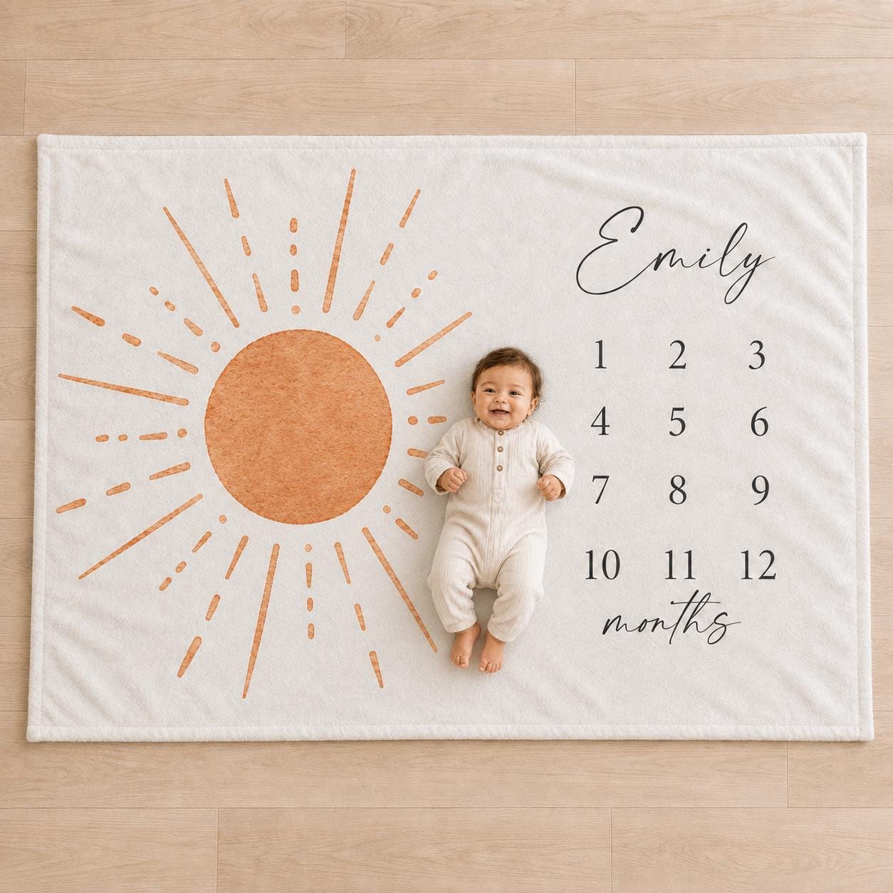 Personalized sun milestone blanket. Smiling baby lying on a personalized sun milestone blanket with terracotta watercolor rays and numbers 1 through 12.