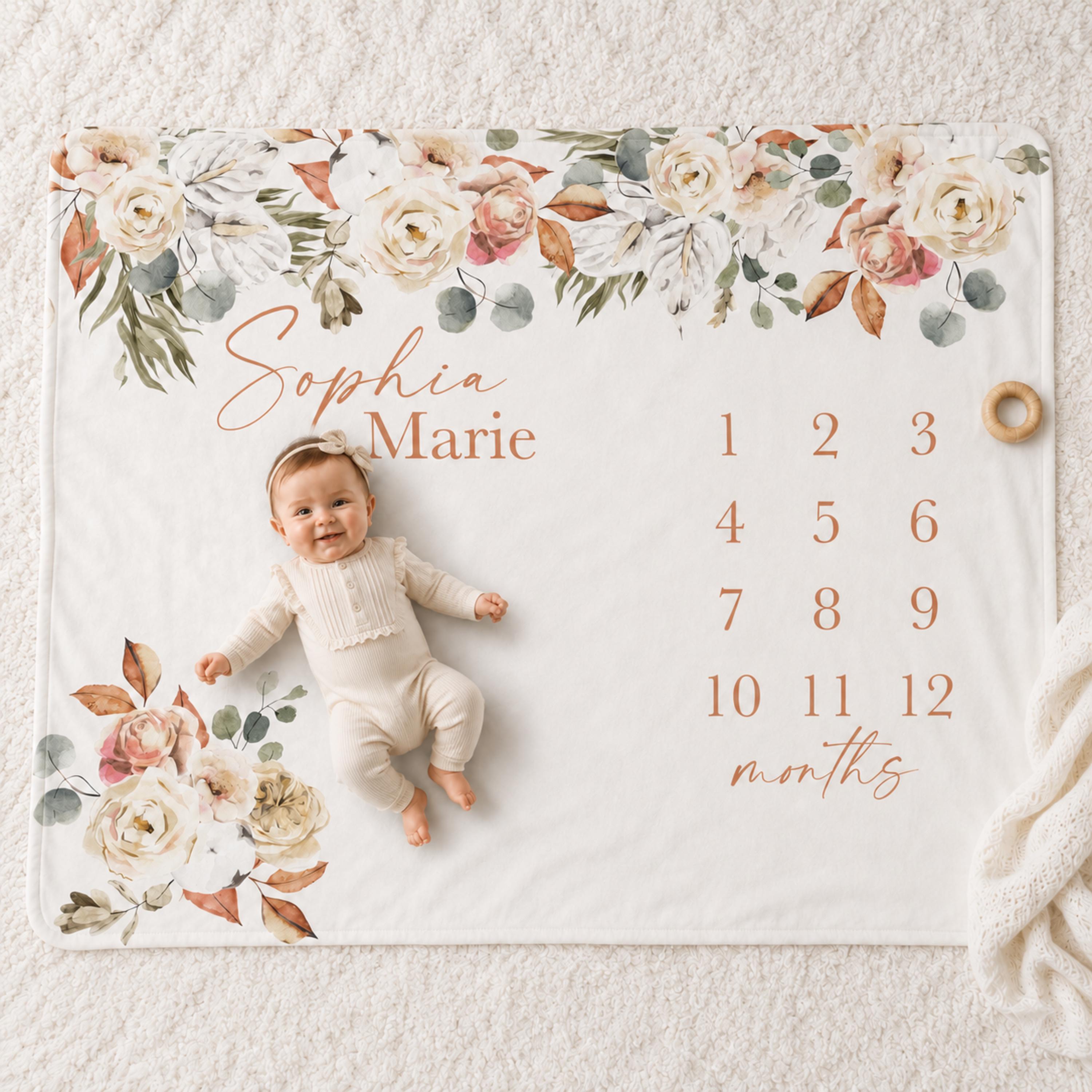 A cheerful baby lays smiling on a fall themed personalized monthly milestone blanket featuring an earth tone Terracotta Rose & Neutral Eucalyptus Boho floral border with the name "Sophia Marie" printed on it.